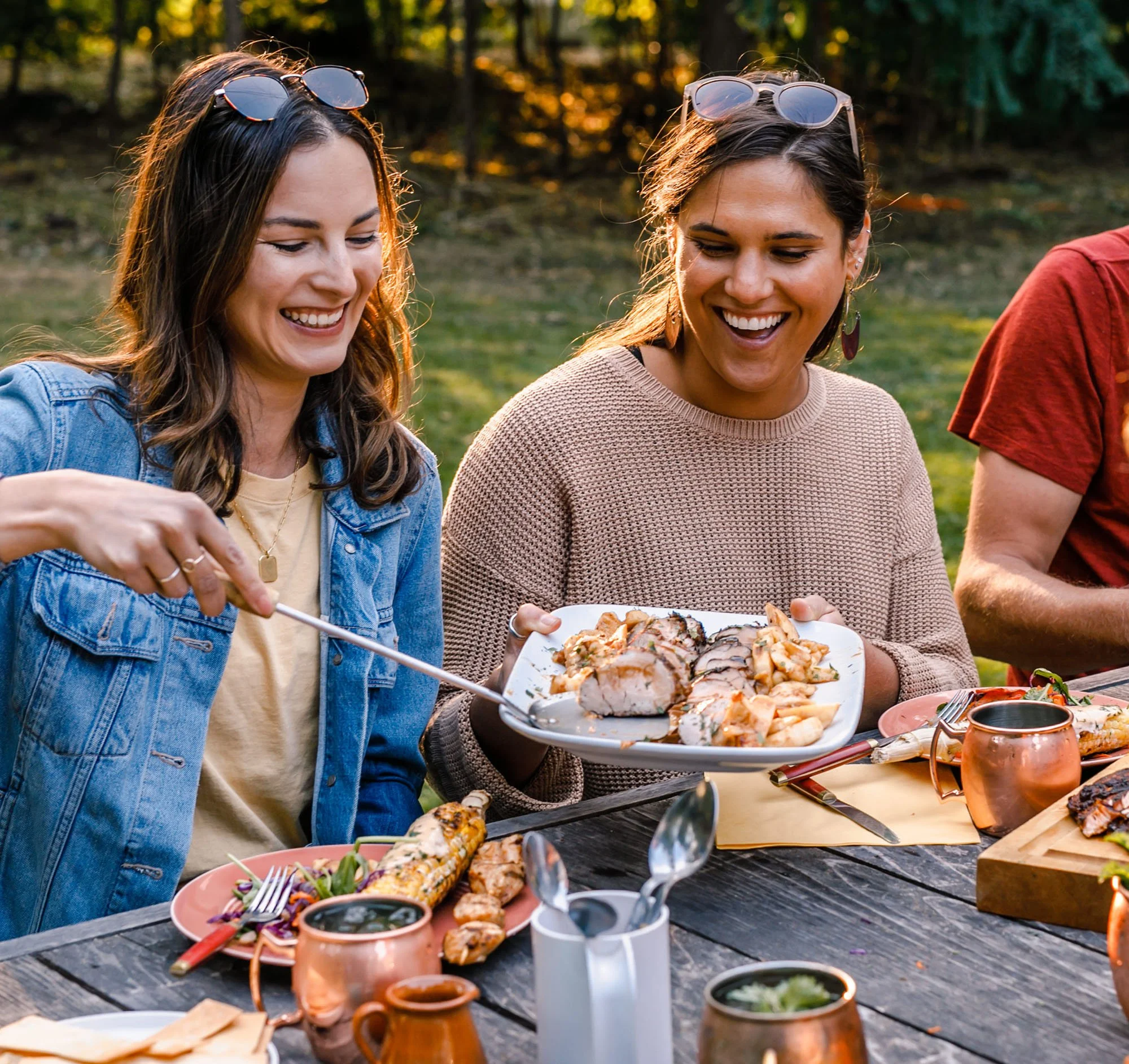 Friends sharing food over a picnic table on a summer evening.