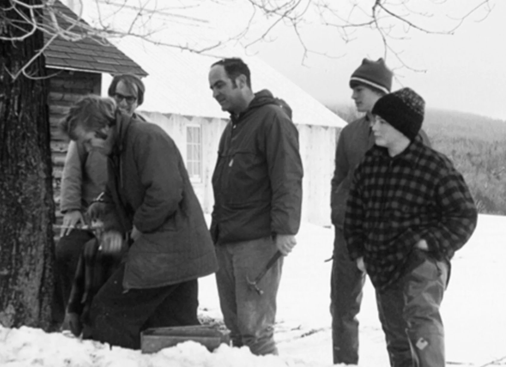 A historical black and white photograph of David Marvin tapping a maple tree.