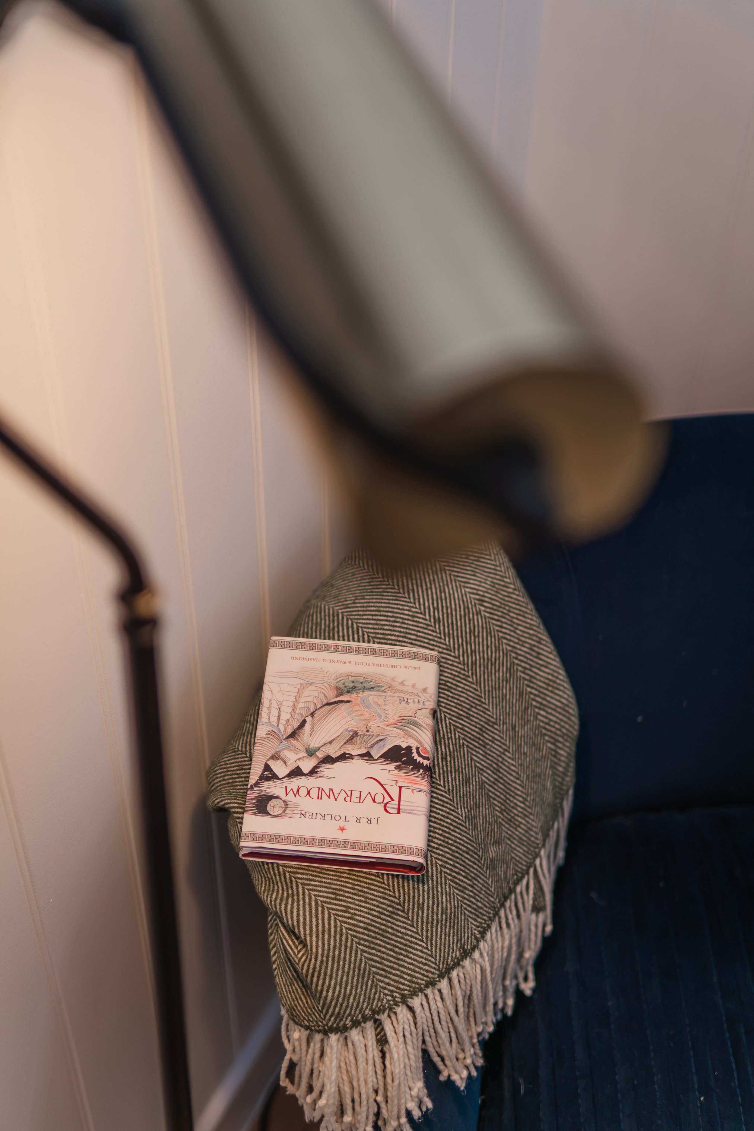 A person wearing plaid pants sitting on a train with a book titled 'Povera Dom' resting on their lap, with a white wall and part of a door visible in the background.