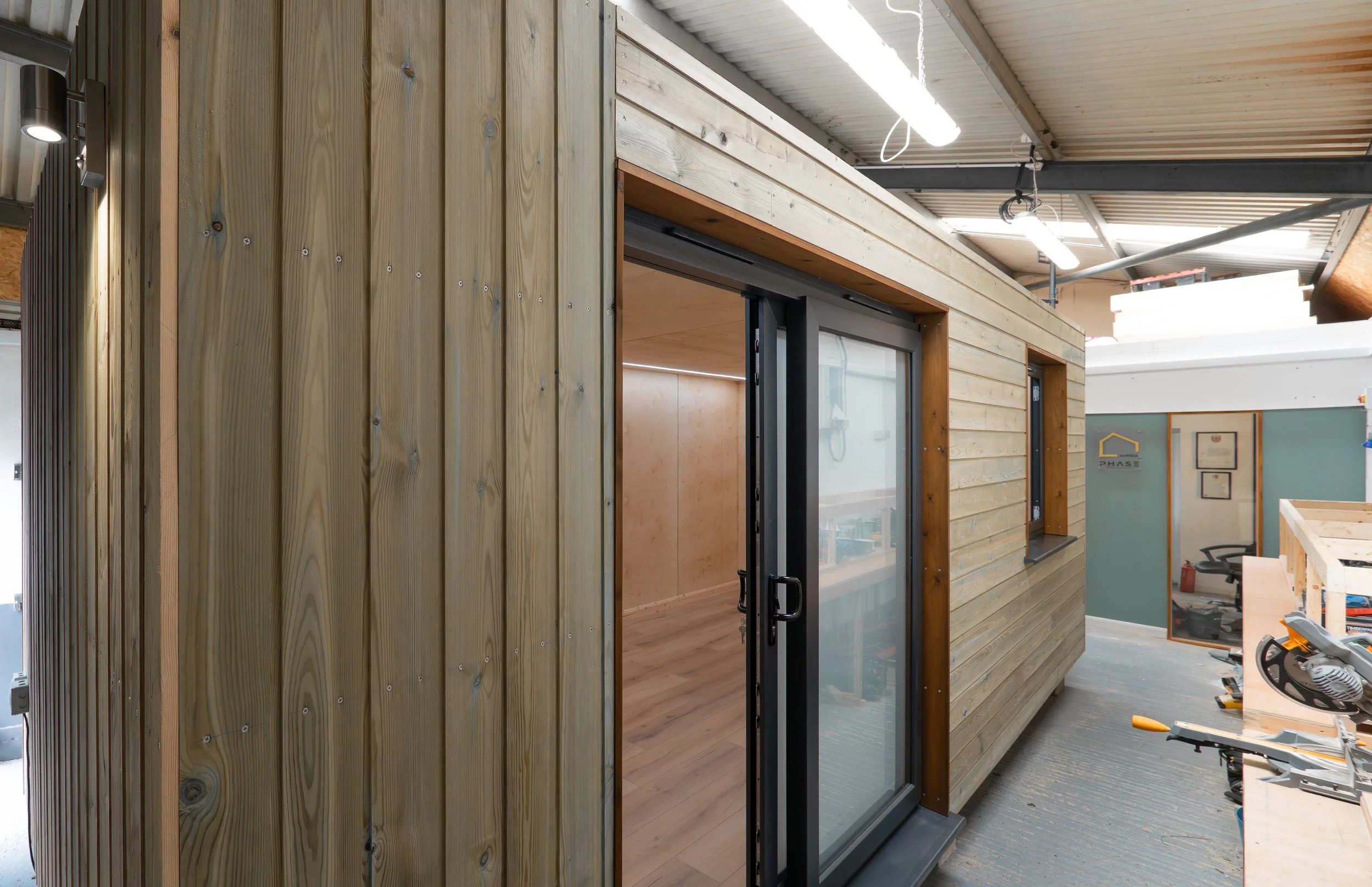 A wooden structure with sliding glass doors in a workshop or construction space, with tools and materials around.