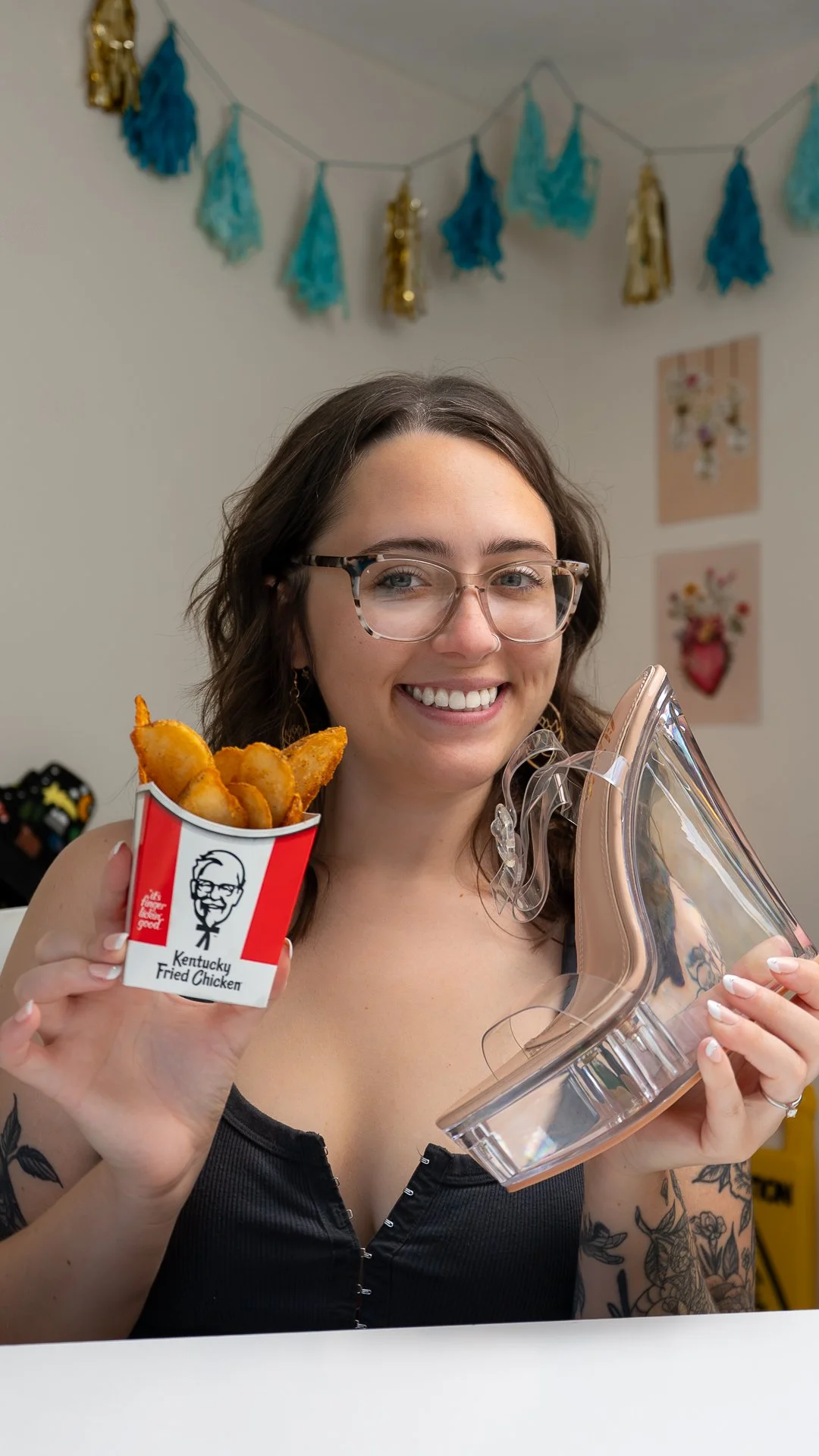 Smiling artist Mikaela from Sneaker Queens Customs holding KFC potato wedges and clear platform heel from KFC wedge comeback campaign.