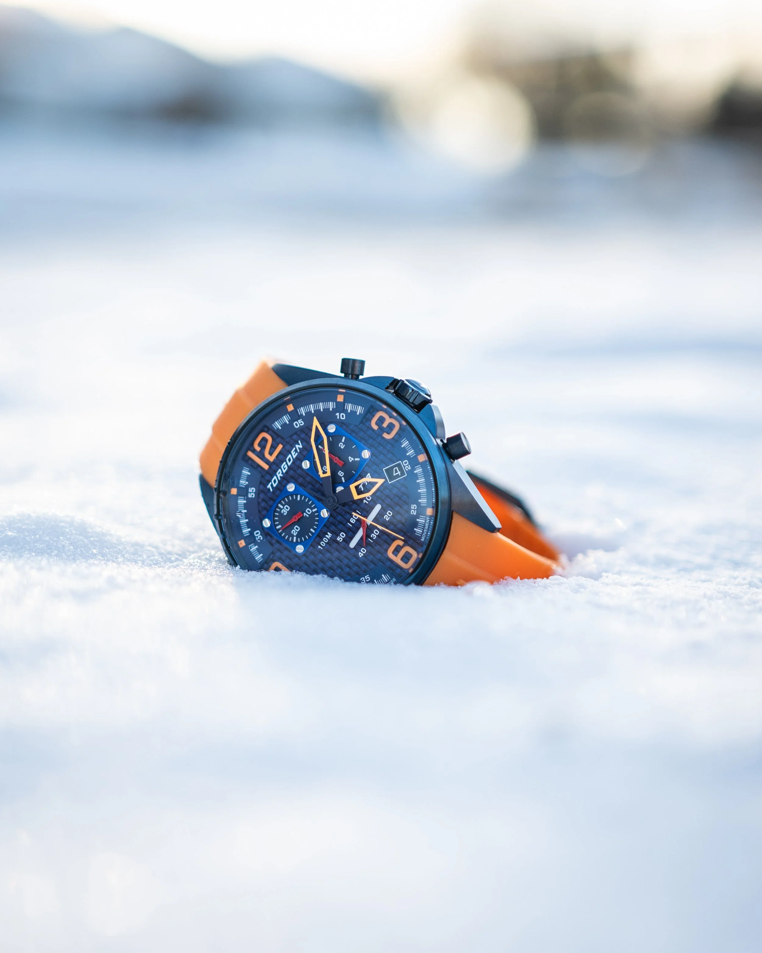 Torgoen T18 blue dial watch with orange strap resting in snow, outdoor lifestyle product photography.