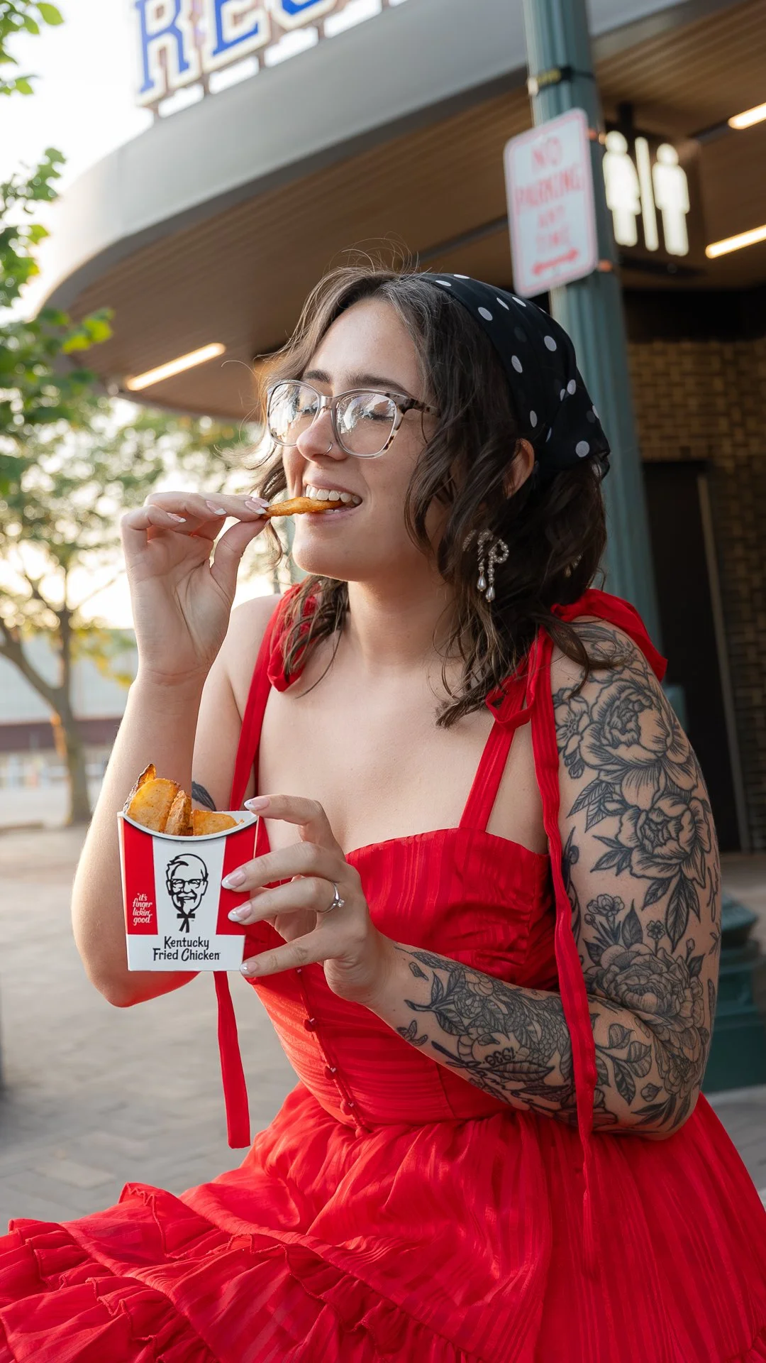 Woman in red dress eating KFC potato wedges outdoors, lifestyle photography for KFC x Sneaker Queens Customs campaign.