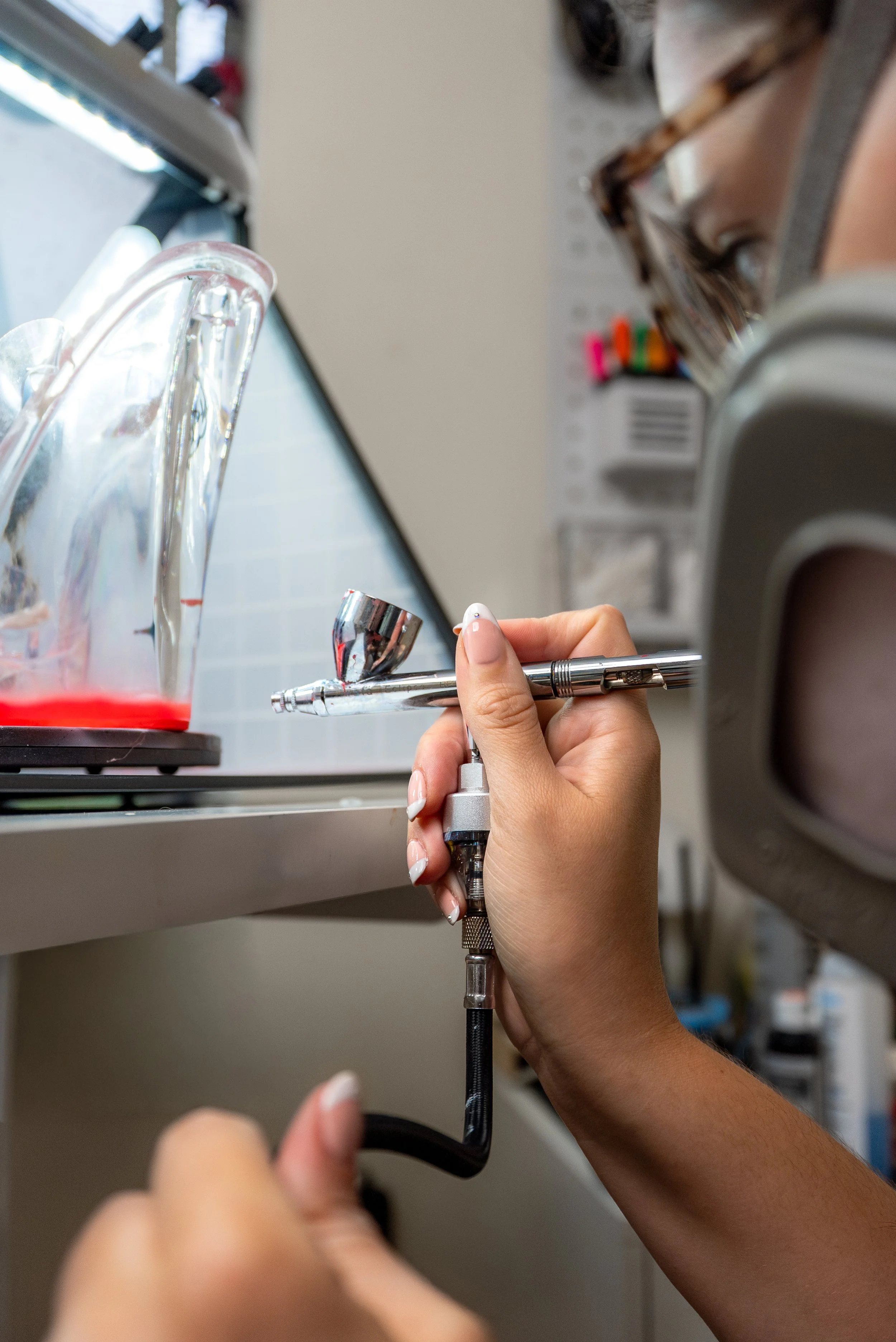 Artist airbrushing red paint onto clear platform high heel for KFC potato wedge custom shoe collab with Sneaker Queens Customs.