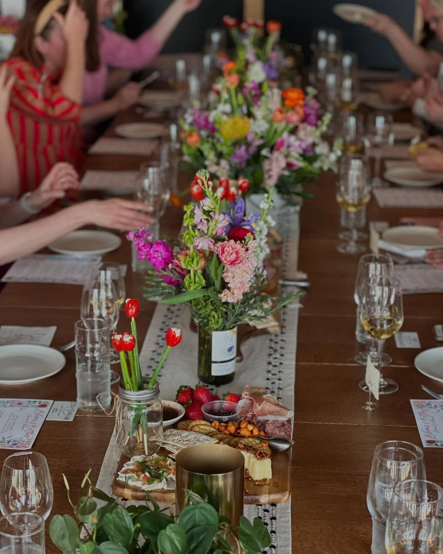 A decorated dining table with flowers, food, and drinks, surrounded by people celebrating.
