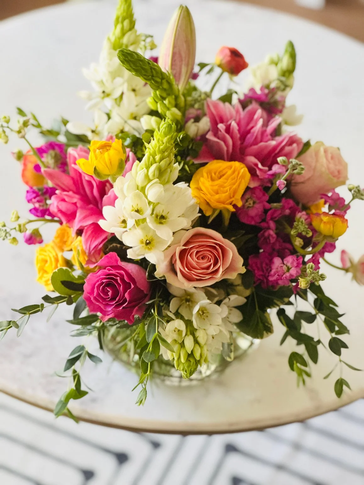 A colorful flower arrangement in a glass vase on a white table.