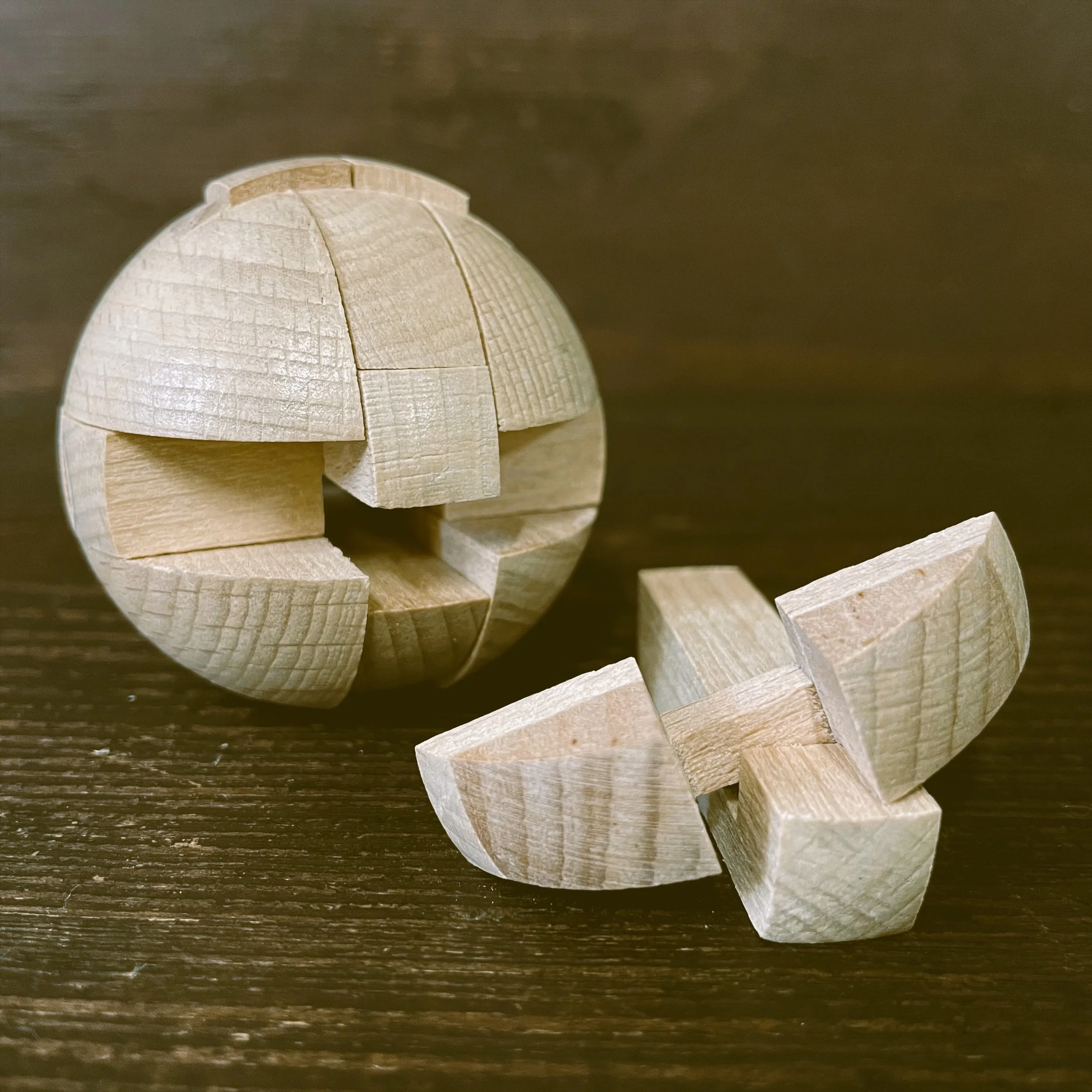 A close-up view of a spherical wooden puzzle or sculpture made of small interlocking wooden pieces on a dark wooden surface.