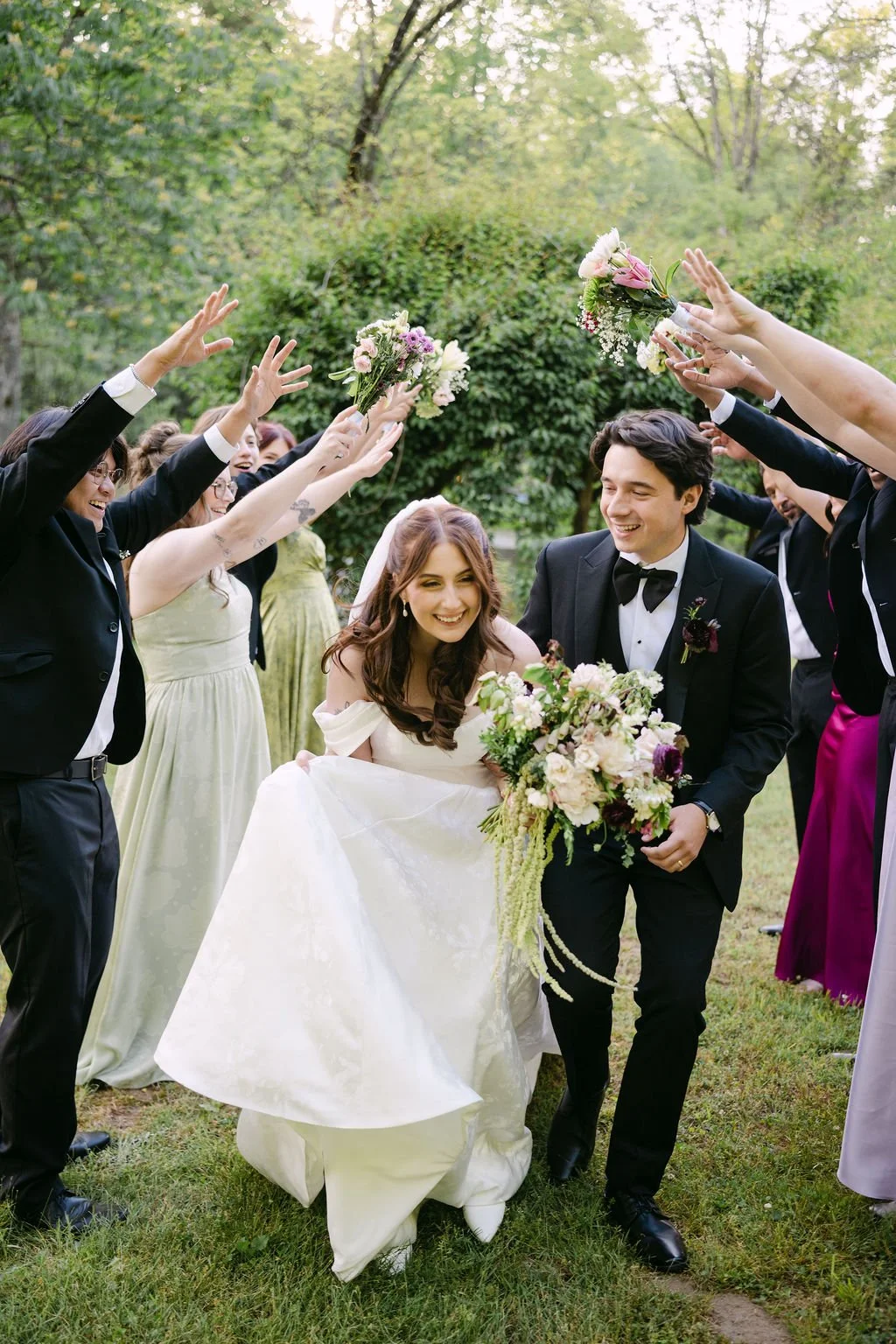 A bride and groom walking together outside, surrounded by friends and family throwing flower bouquets in celebration.