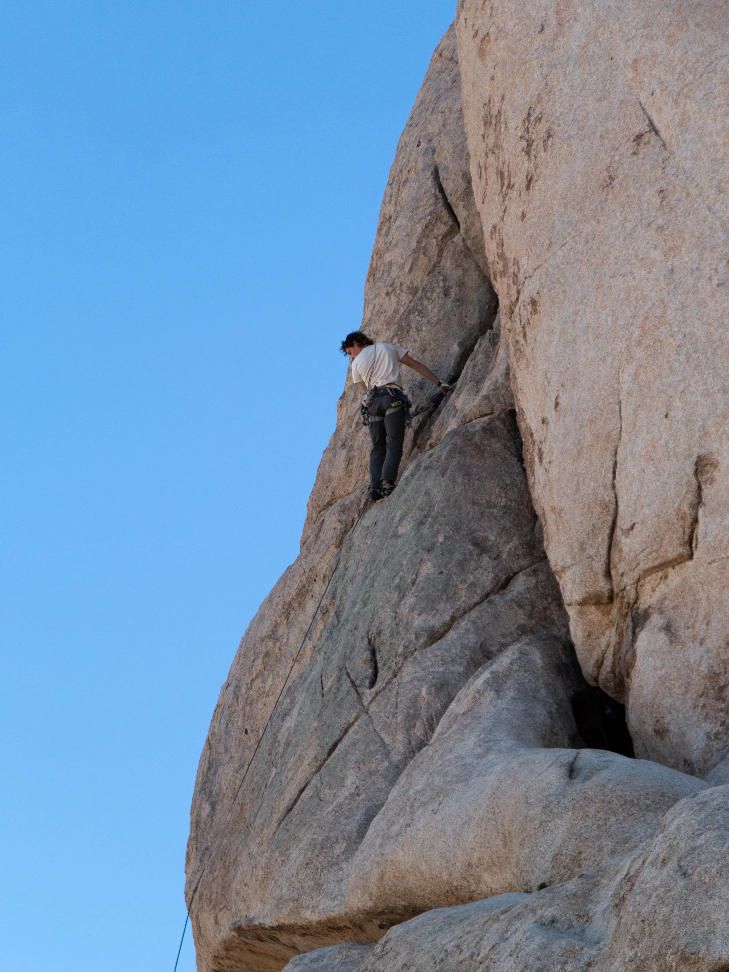 Person rock climbing on a large rock face with blue sky background.