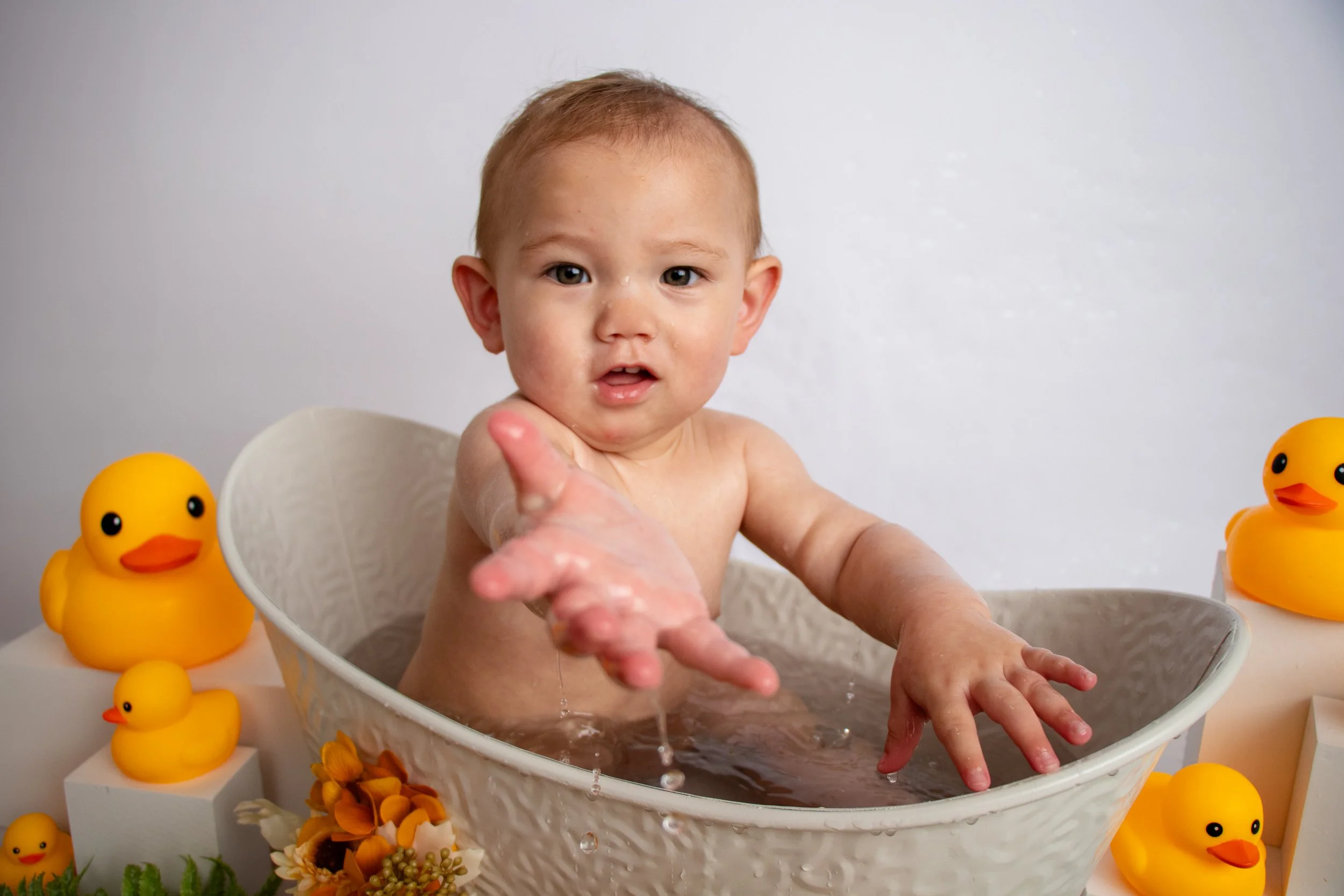 A young child bathing in a white tub surrounded by yellow rubber ducks and floral decorations. (Wobbler Splash Session)