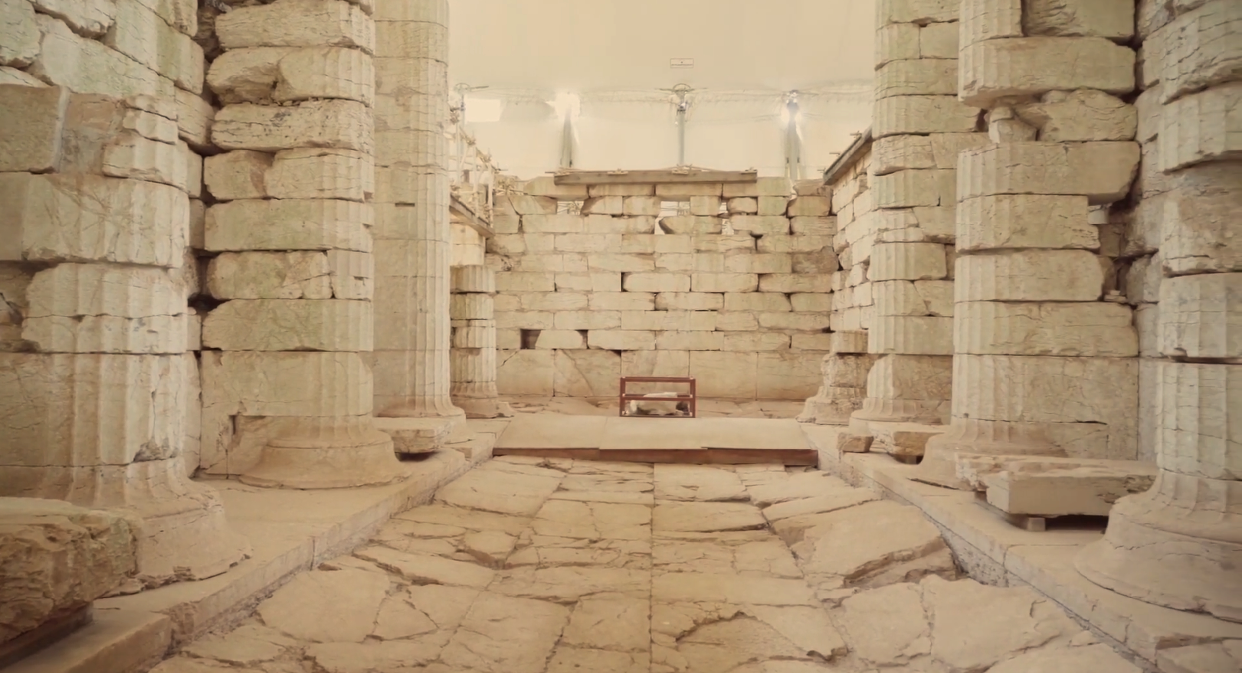 Ancient ruins with stone columns and brick walls, illuminated from above with a few modern light fixtures.