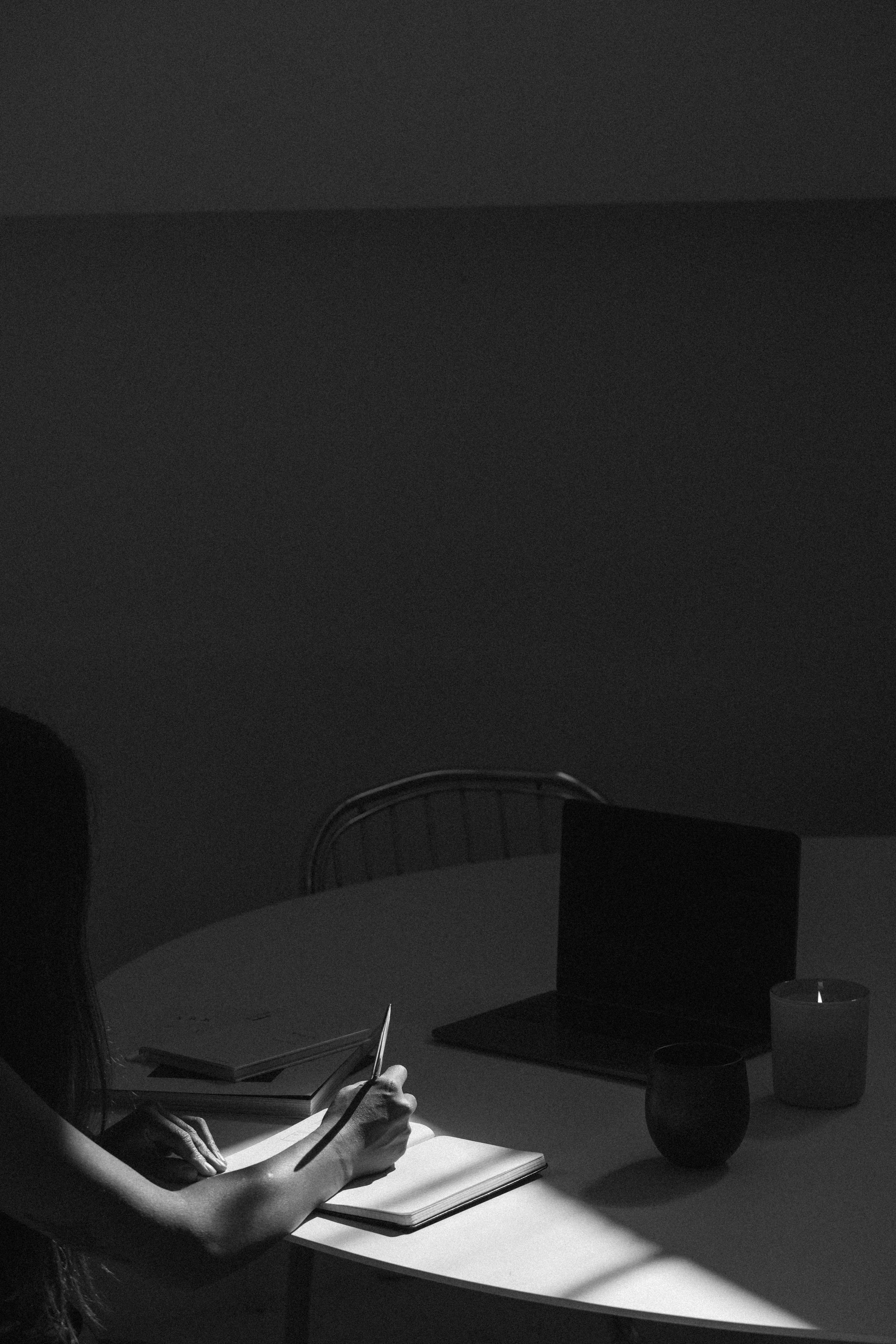 Black and white photo of a desk with a closed notebook, a stone on top of it, a pen, and papers with printed text and graphics.