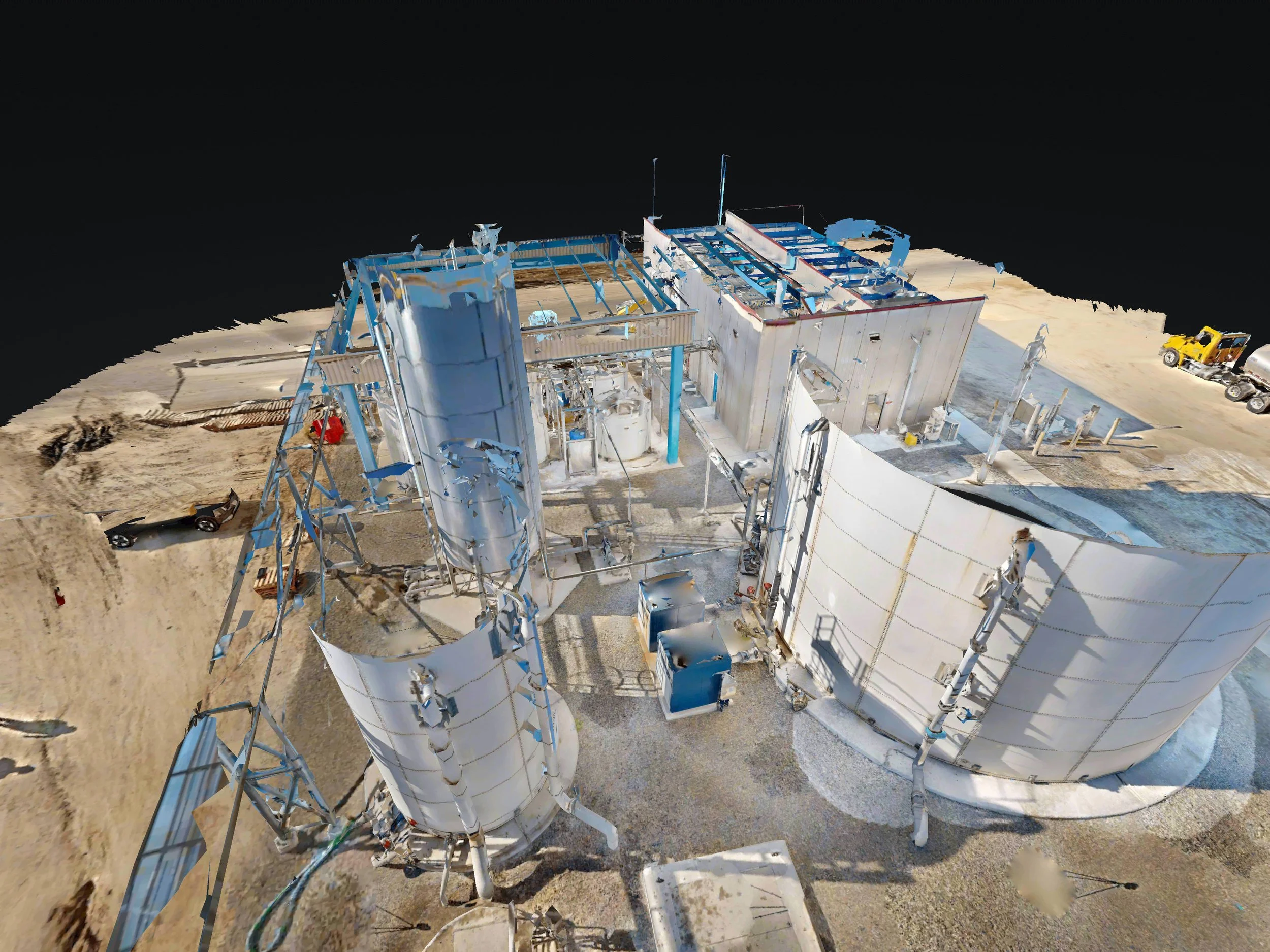 Aerial view of a construction site with large white metal structures, machinery, and vehicles on sandy ground.