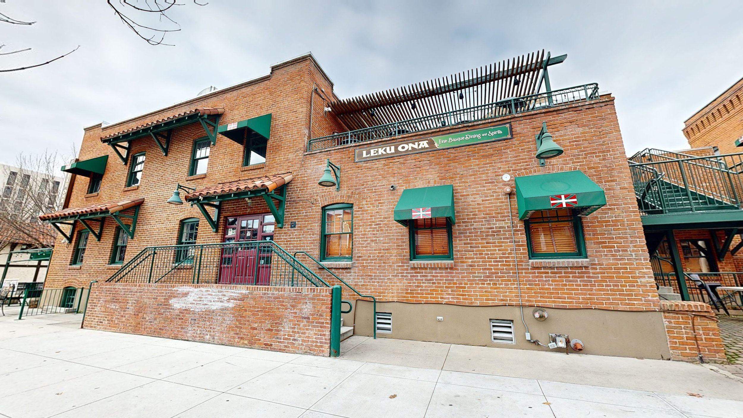 The exterior of a brick building with green accents, awnings, and a sign that reads 'Leku Ona' and 'Fine Basque Dining and Spirits.'