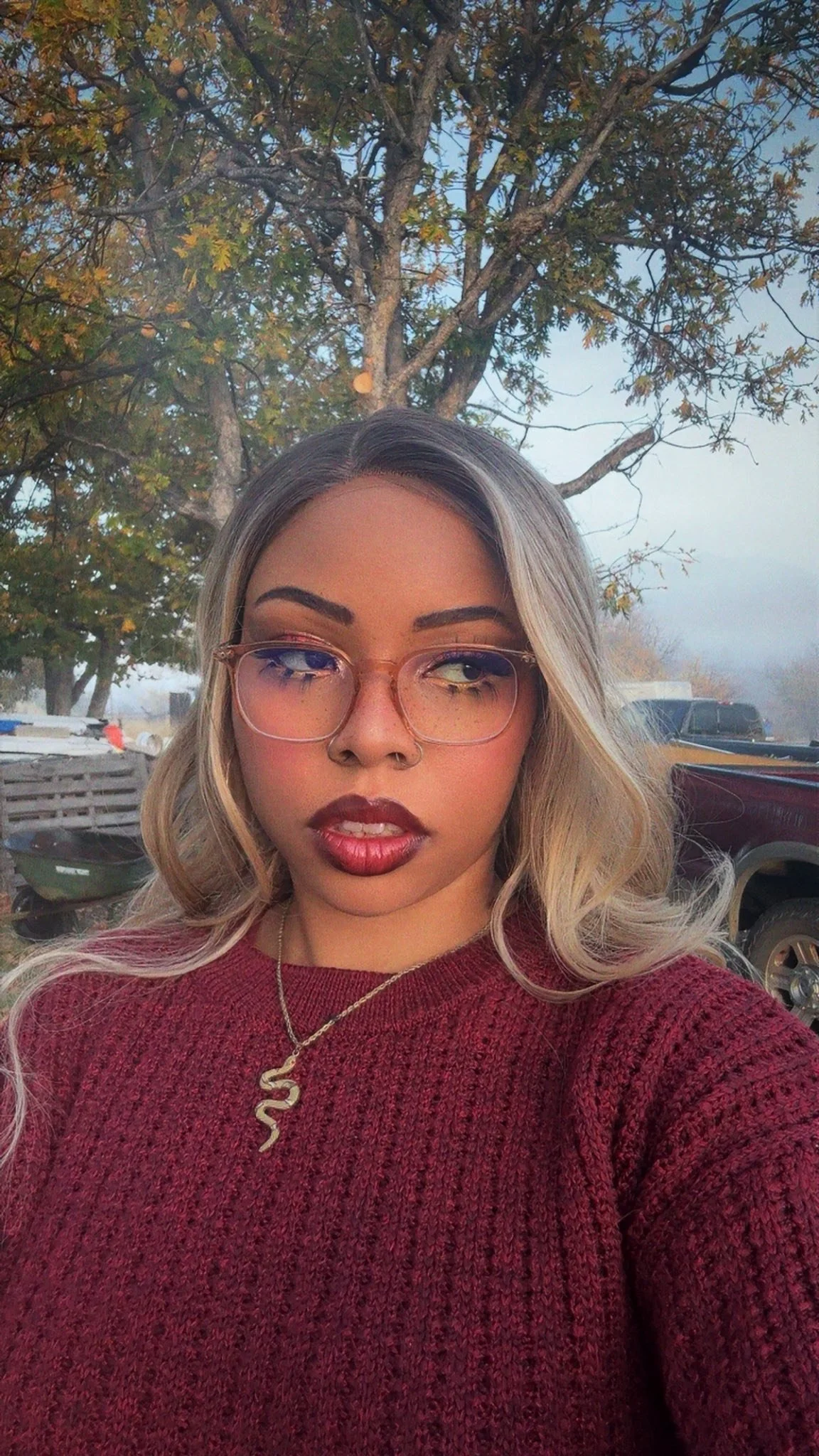 Mani Da Brat independent female hip-hop and R&B artist with blonde hair wearing glasses and maroon sweater outdoors at sunset