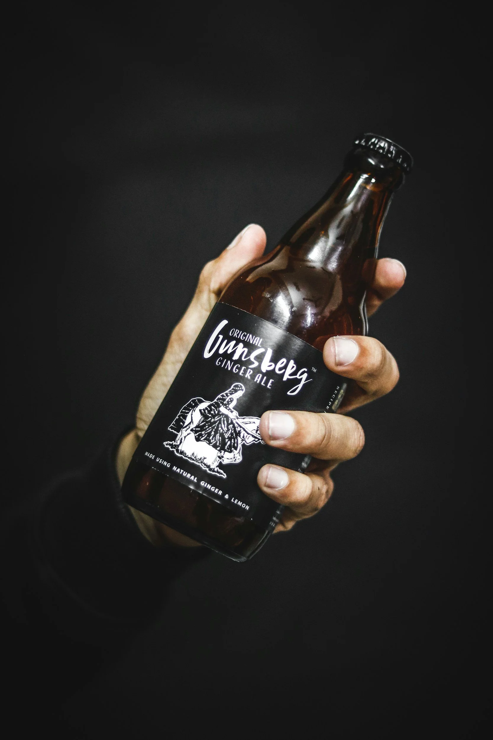 A person holding a brown glass bottle of Untzberg Ginger Ale against a black background.
