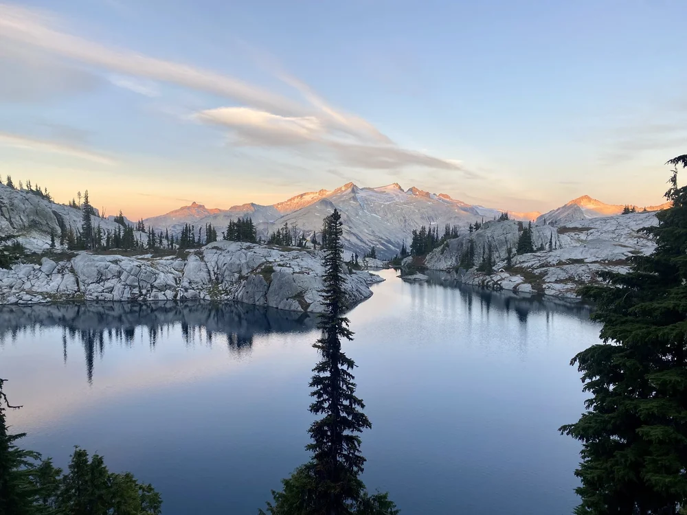 Alpenglow lighting the peaks above a still alpine lake in the North Cascades