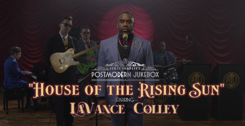 Cast of 'House of the Rising Sun' from Scott Bradlee's Postmodern Jukebox perform on stage with instruments, featuring a man in the center with a microphone in front of a red curtain.