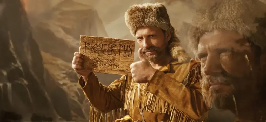 A man dressed as a prospector in a wilderness setting, holding a wooden sign with writing, with a rugged background and a superimposed face of another man with glasses and a furry hat.