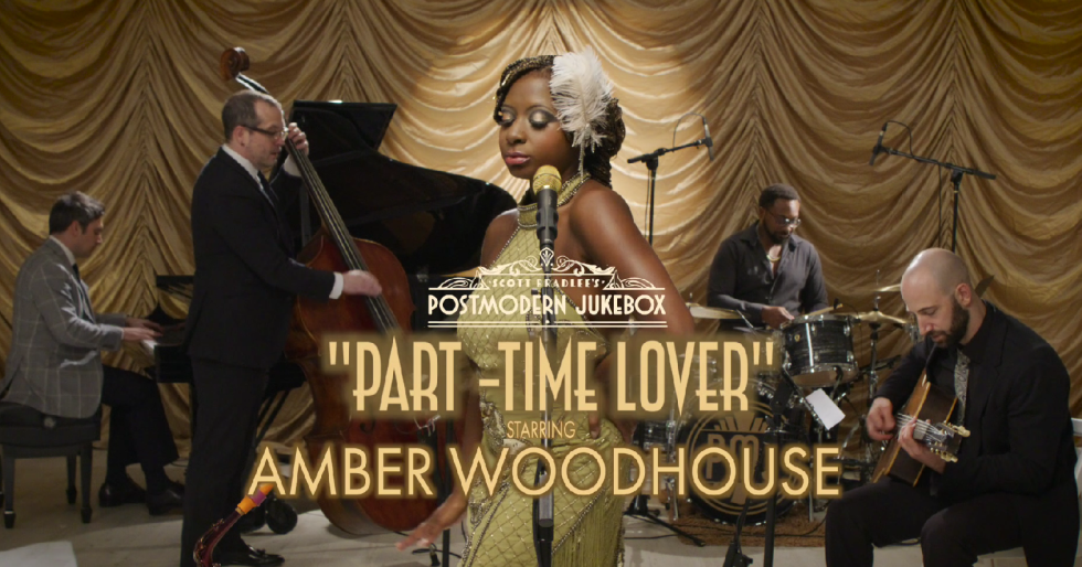 A band performing on a stage with a golden curtain backdrop, featuring a female singer at the center, a pianist, a double bassist, a drummer, and a guitarist, with overlay text for a music video titled "Part-Time Lover" by Amber Woodhouse.
