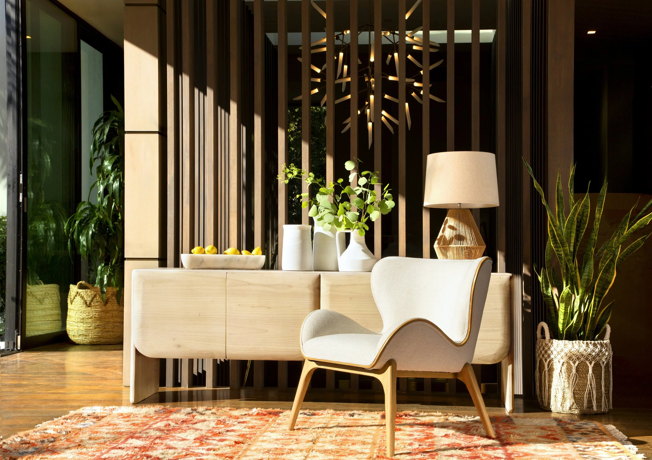 Modern living room with wooden chair, sideboard, and decorative items, including plants, a lamp, and a bowl of lemons.