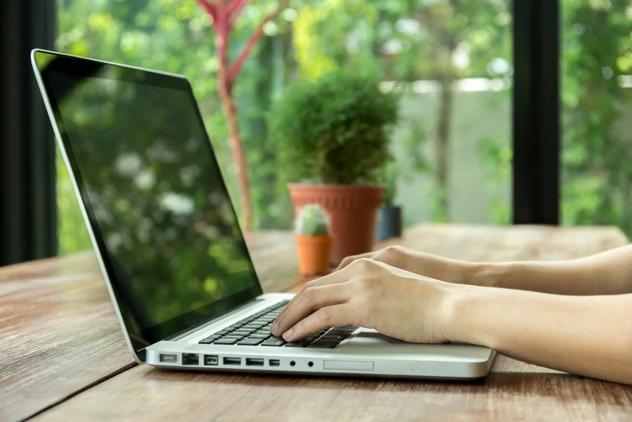 Hands typing on a laptop in a bright, natural light workspace, representing focus and attention in modern digital life