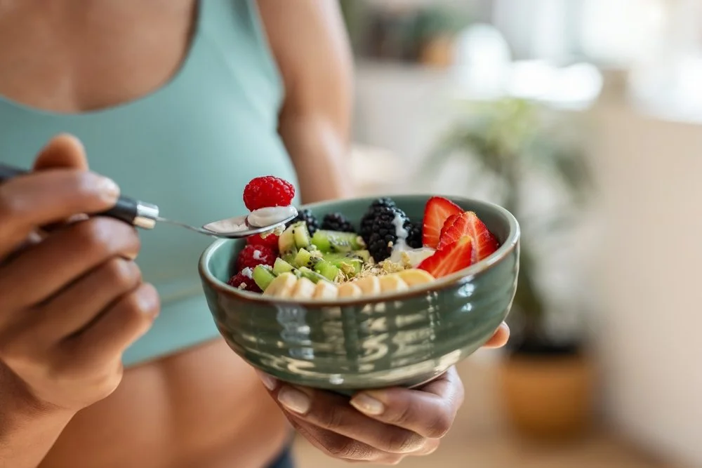 Woman holding a healthy breakfast bowl with fruit and yogurt, representing balanced nutrition and meal timing