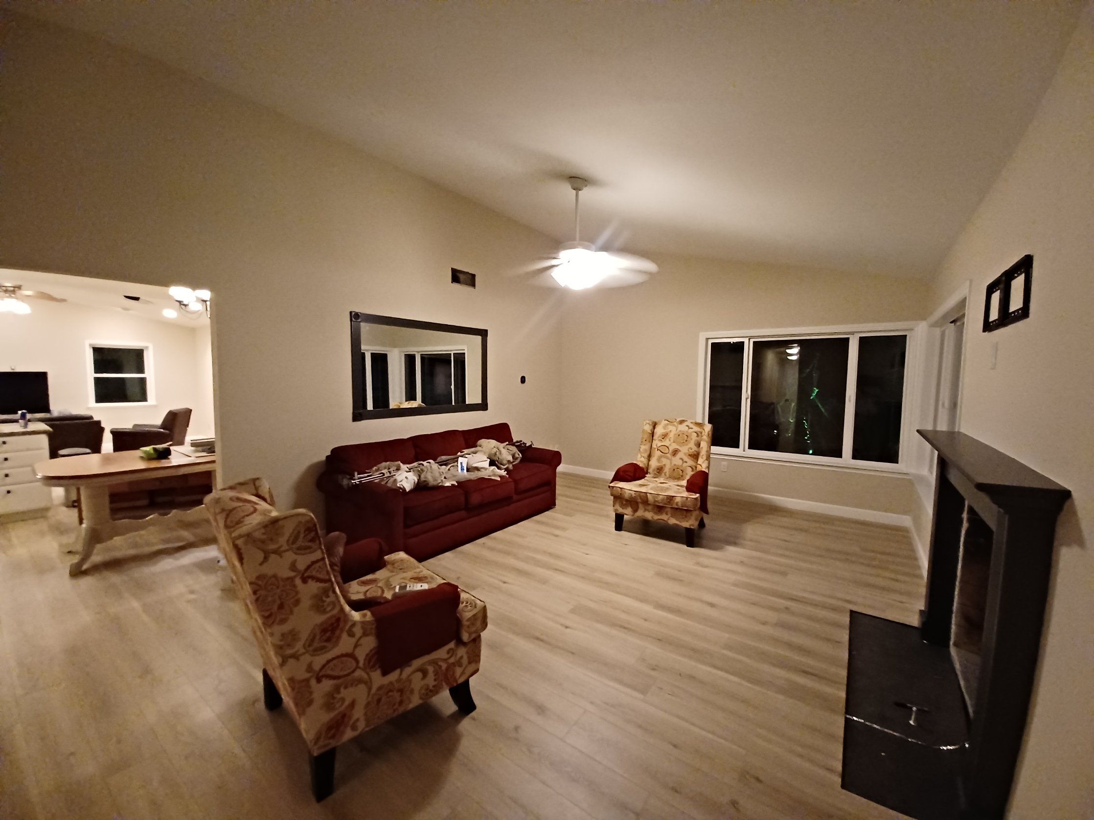 Interior paint walls baseboard in Poway. Living room with a red sofa, two patterned armchairs, a ceiling fan with light, a large window, and a TV on a stand.