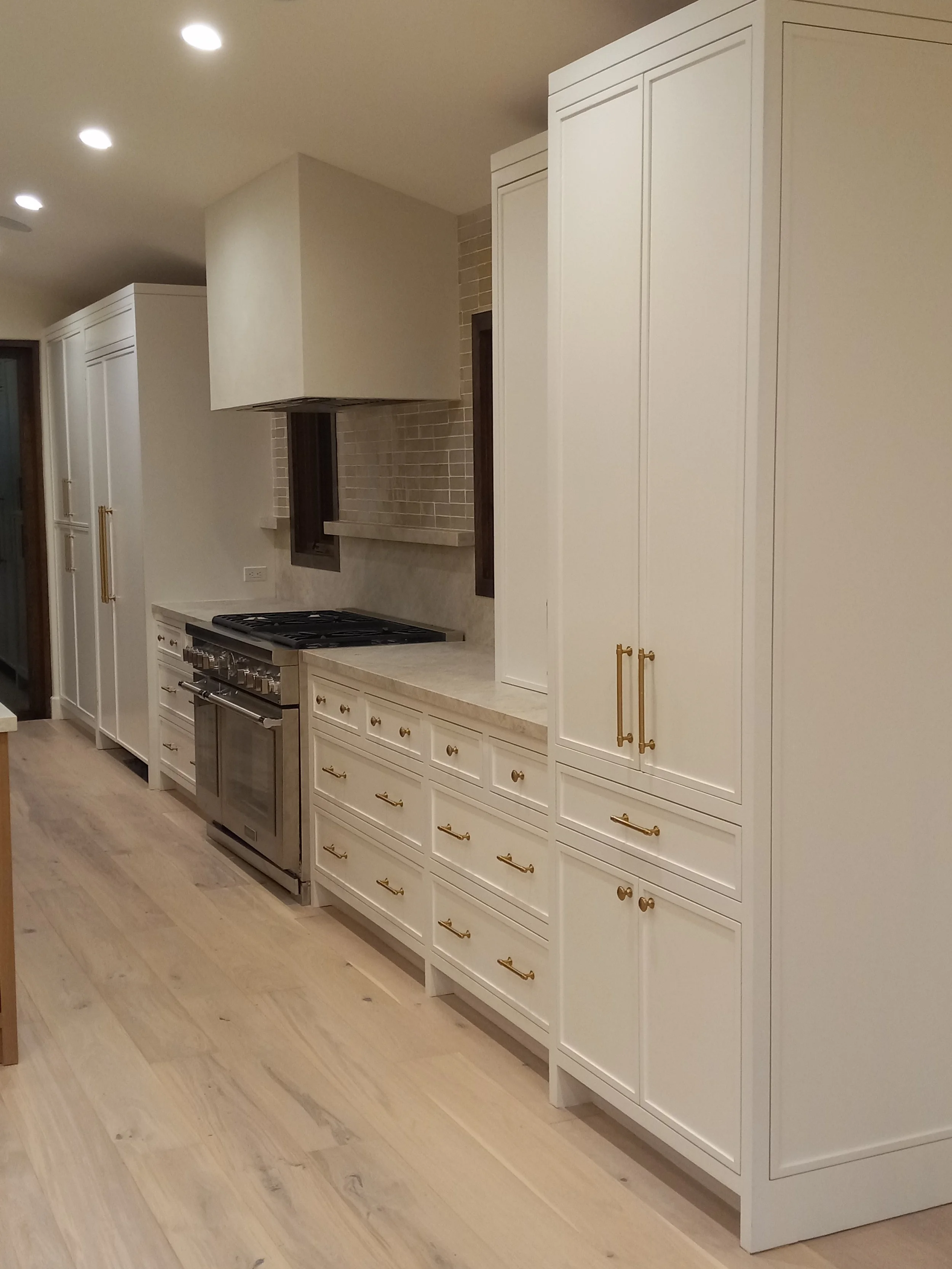 Modern white kitchen with gold hardware, built-in cabinets, a large oven, and a beige countertop.