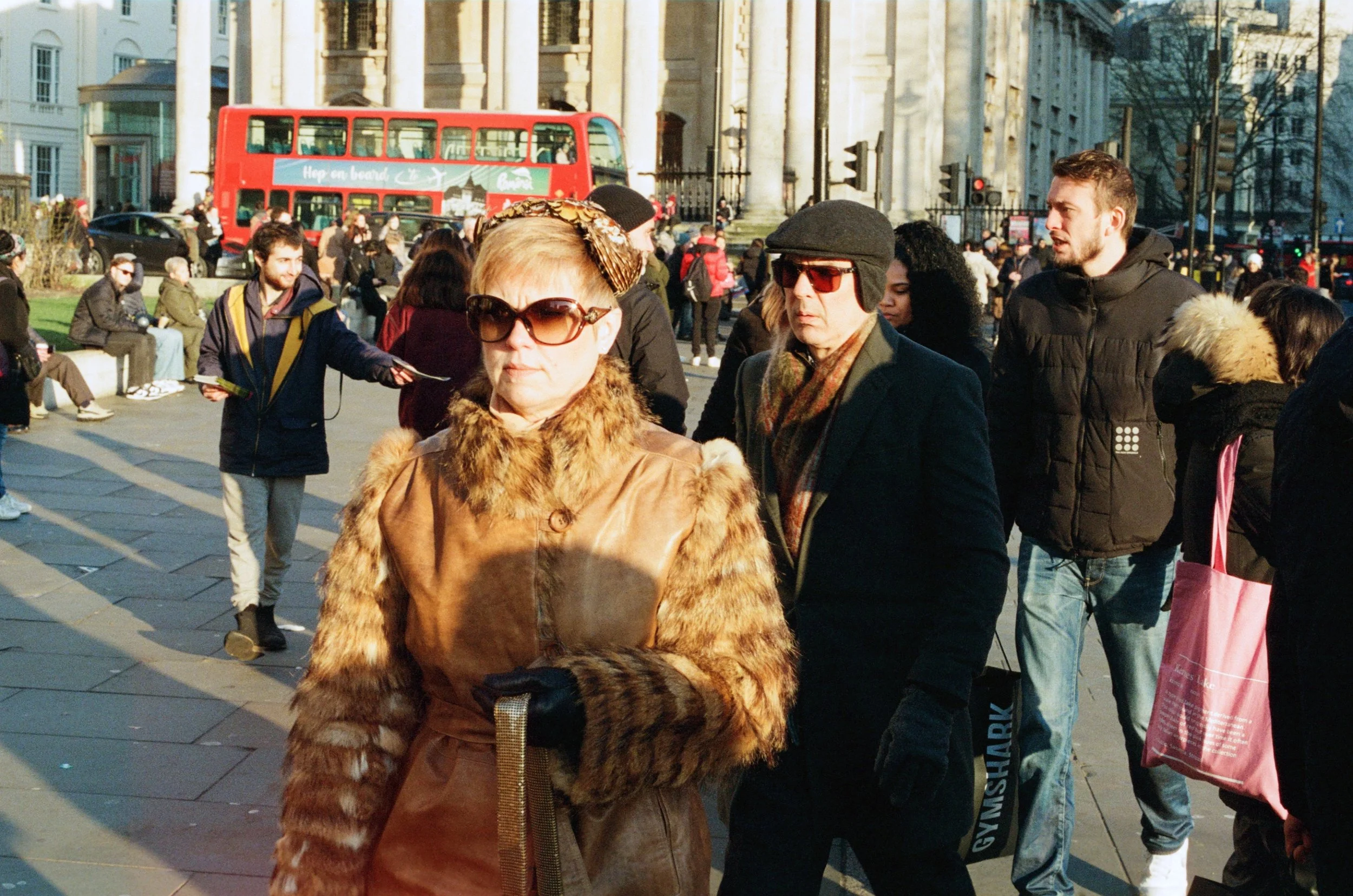 Bold analog film street portrait of an elegantly dressed woman in a fur coat and oversized sunglasses walking through Trafalgar Square, London, captured by Dario Tapia.