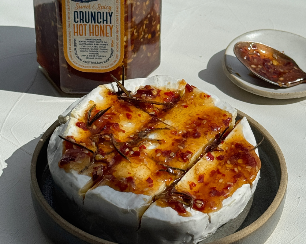  A wheel of brie with rosemary and hot honey with a jar of hot honey in the background 