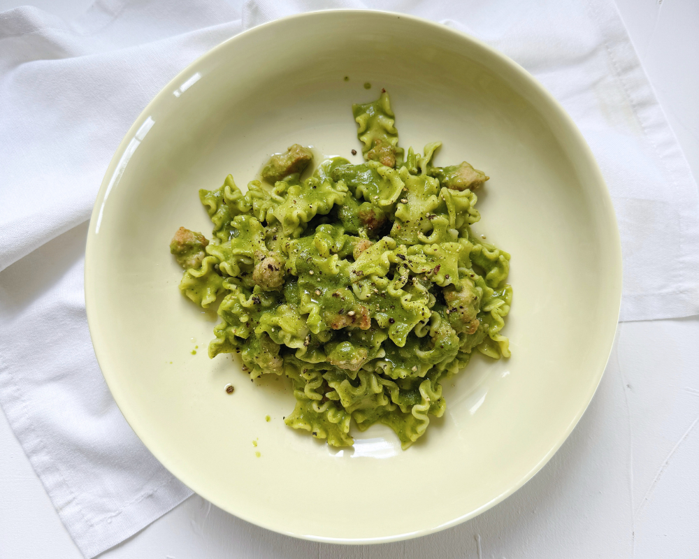  A light yellow bowl against a white background with a creamy, green pasta in the middle 
