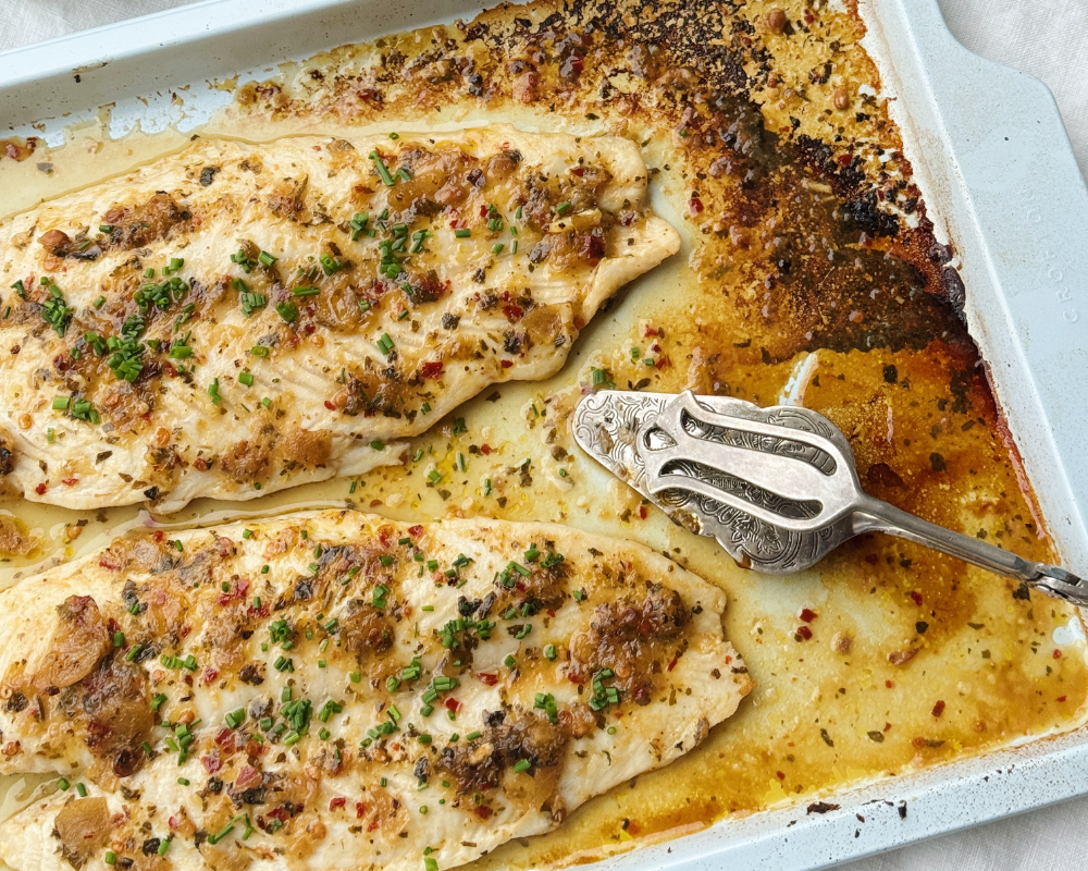  A baking tray with 2 grilled fish fillets topped with lemon chimichurri and fresh chives 