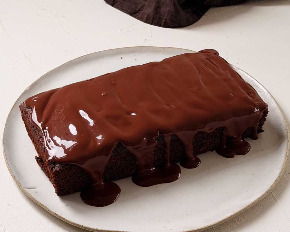  Chocolate loaf cake topped with a glossy dark chocolate ganache drizzle on a white ceramic plate 