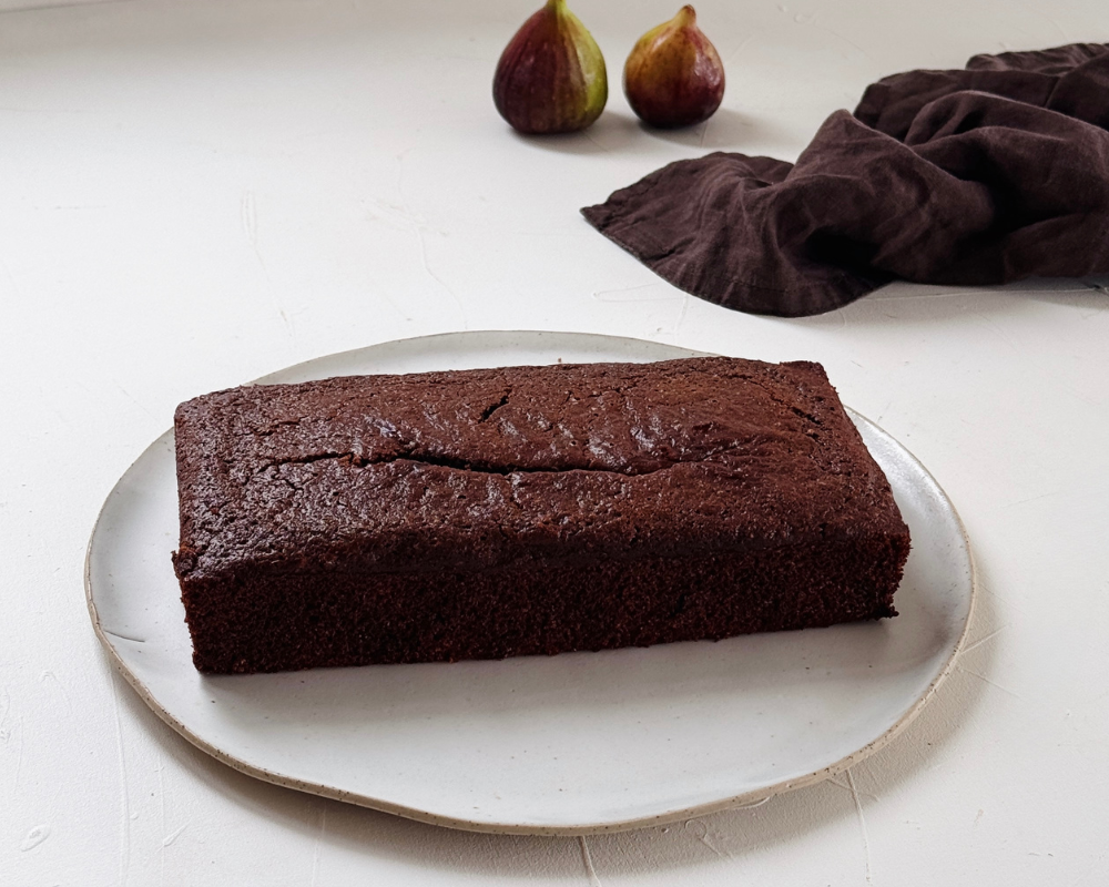  Freshly baked chocolate loaf cake on a white plate with fresh figs in the background 