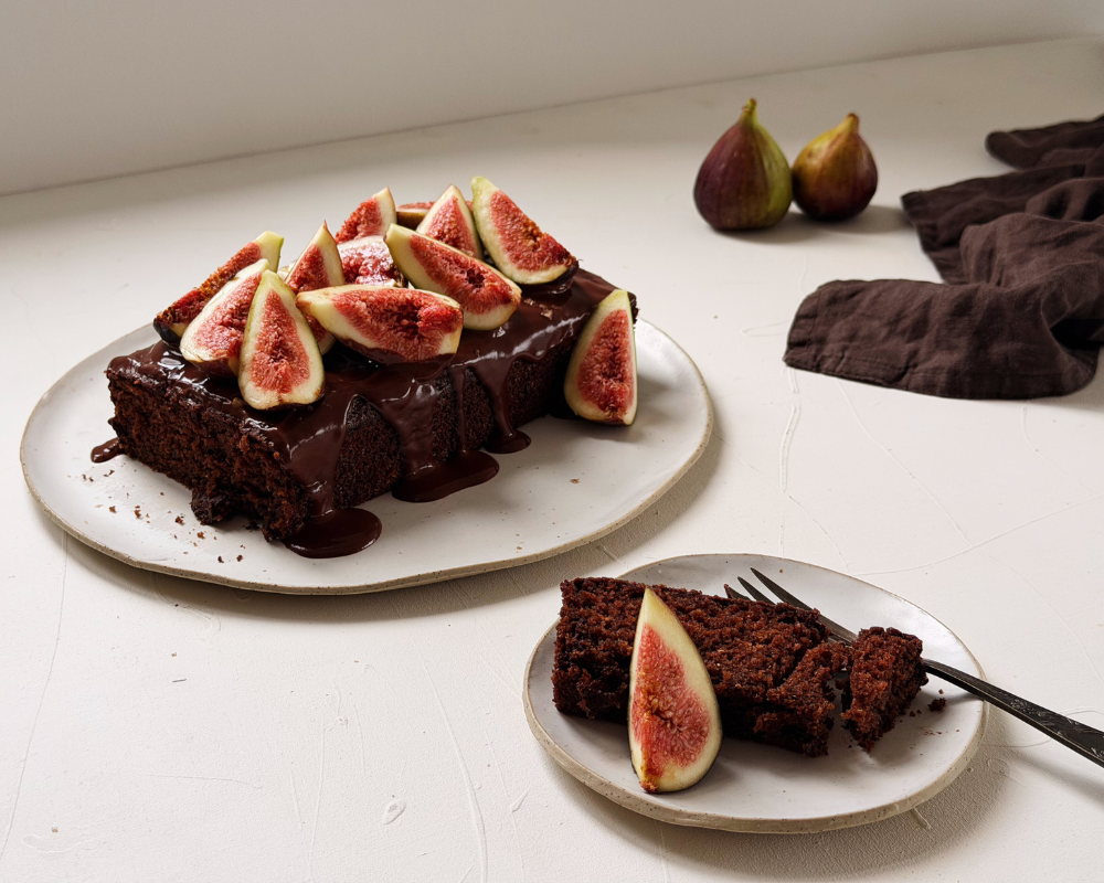  Chocolate fig cake with dark chocolate drizzle and fresh figs on a white plate, with a slice served on a side plate 