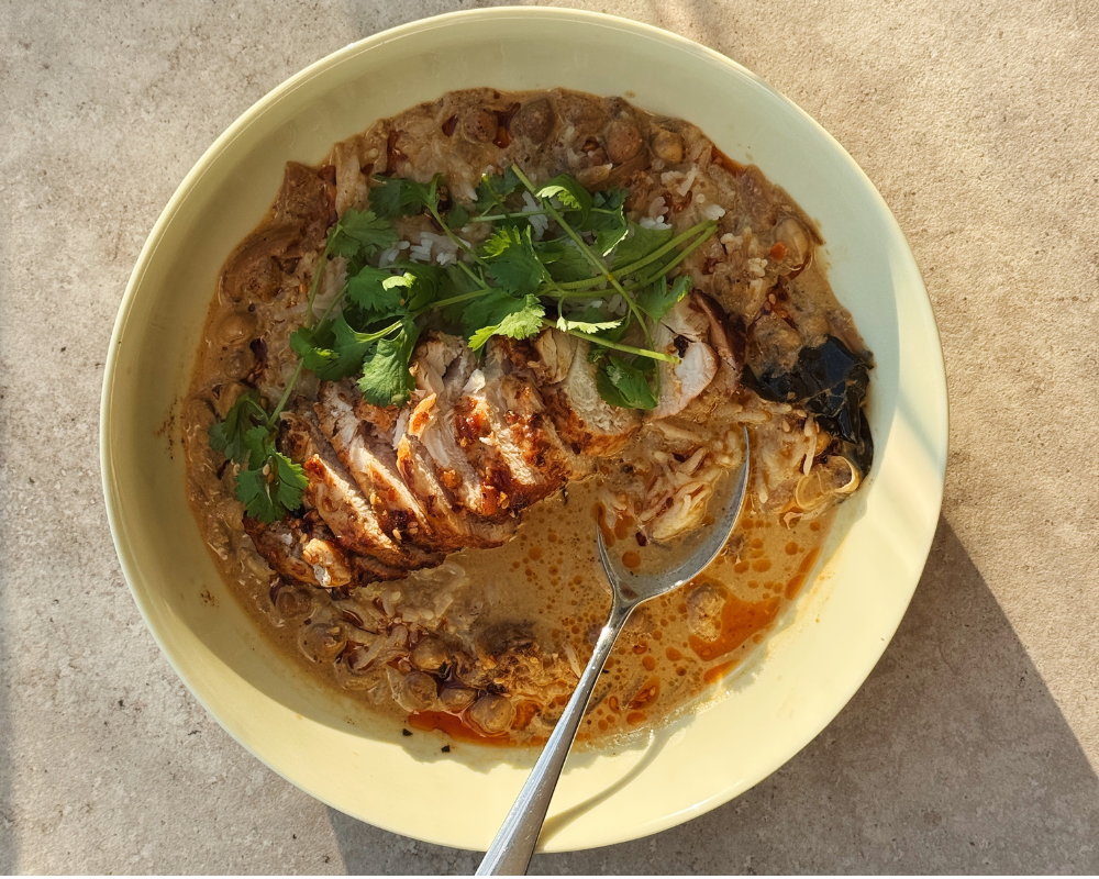  A yellow bowl of brothy coconut curry with chicken and rice topped with fresh coriander and chilli oil  