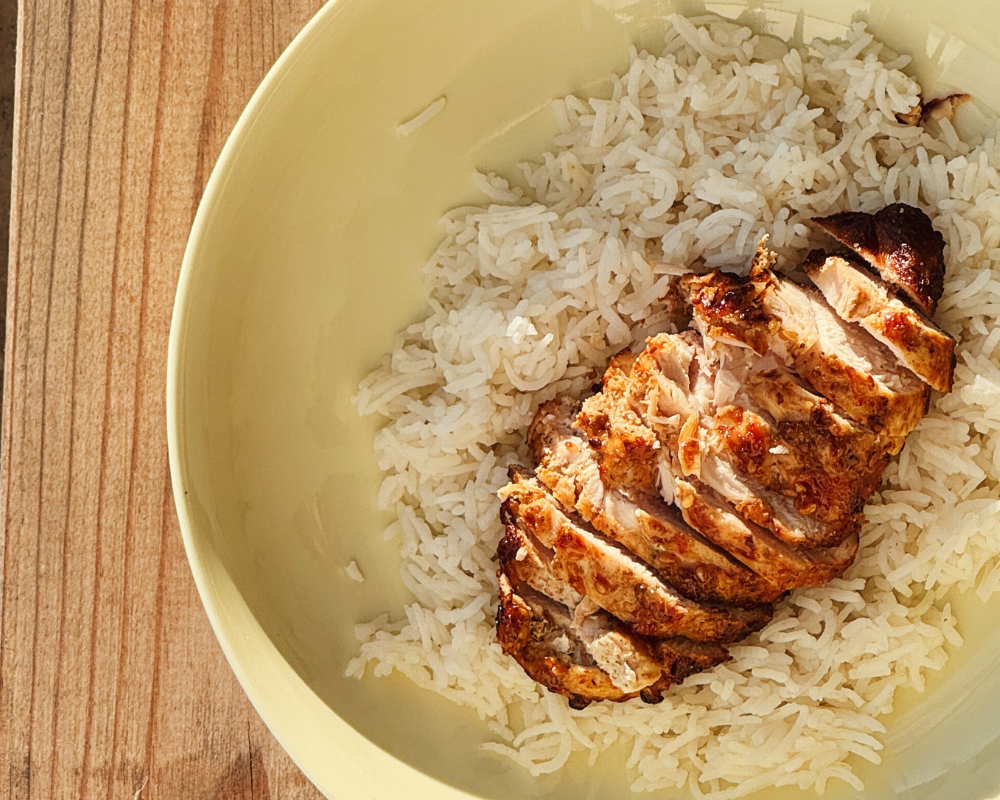  A bowl of steamed rice with grilled chicken waiting brothy coconut curry to be poured 