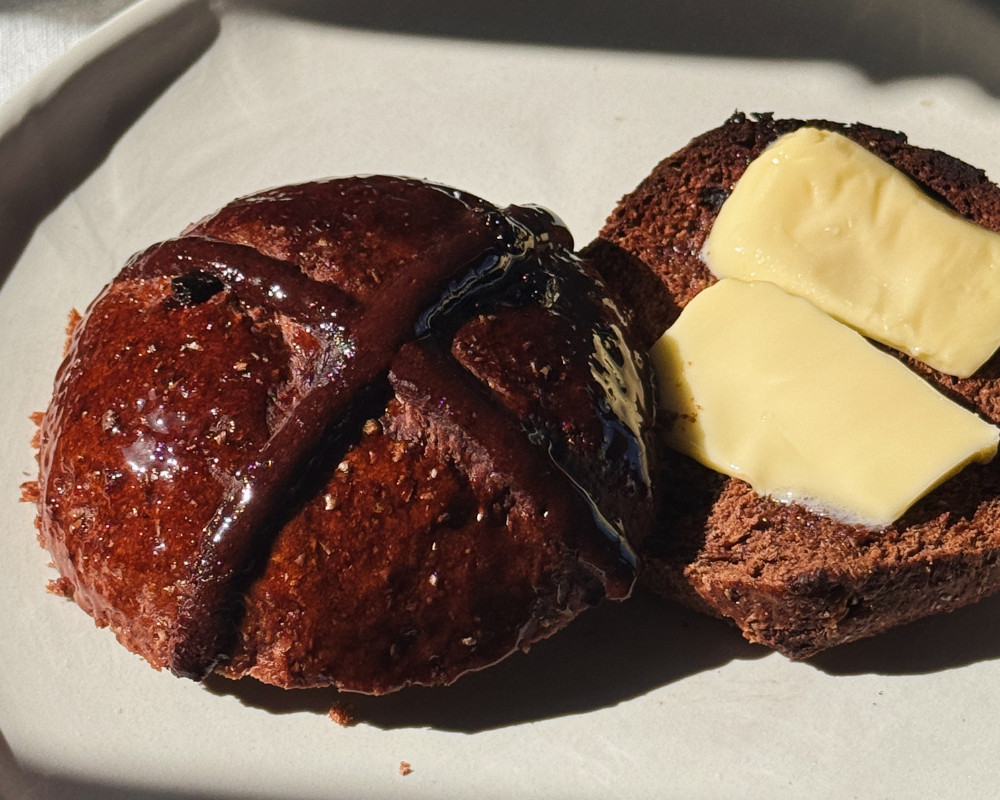  Close up of chocolate cherry hot cross buns on a white plate with thick slices of butter 