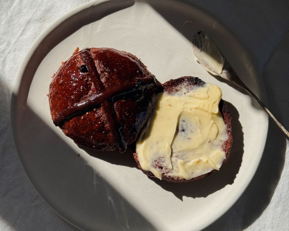  A chocolate cherry hot cross bun spread with melted butter on a white playe  