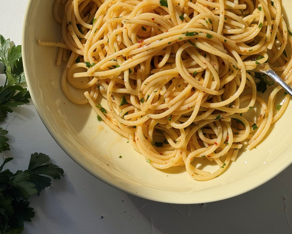  Close up of spaghetti aglio e olio in a yellow bowl with parsley and chilli flakes 