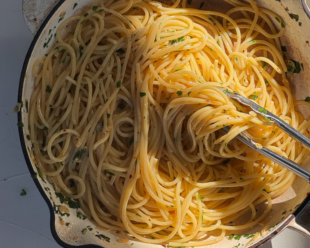  Spaghetti aglio e olio being tossed through garlic and chilli oil in a pan 