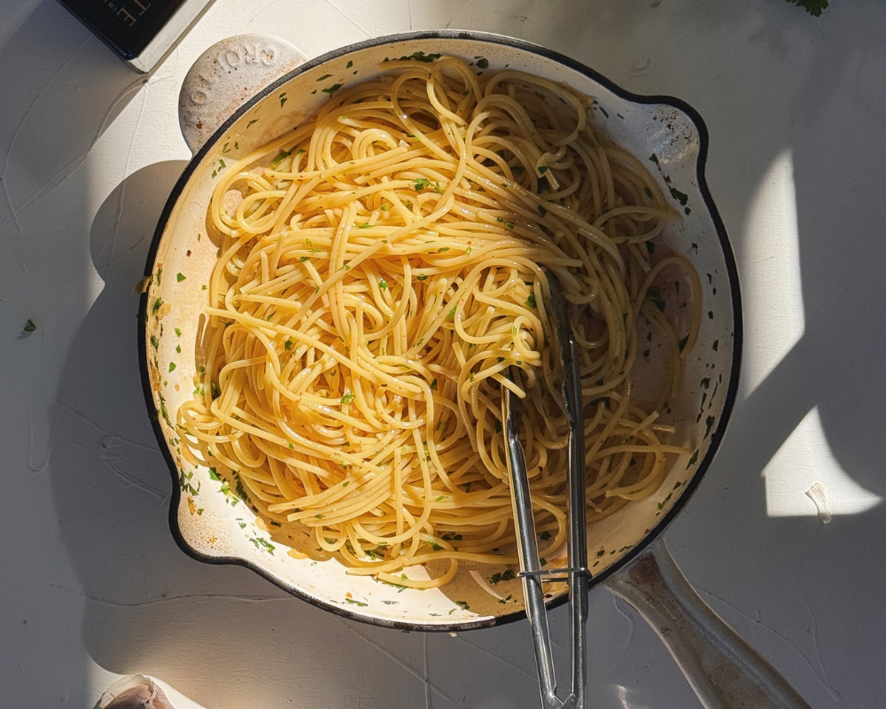  Spaghetti aglio e olio tossed in a white pan with tongs 