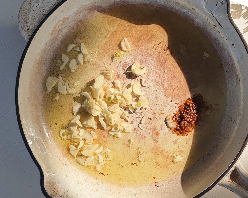  Sliced garlic and chilli flakes blooming in extra virgin olive oil in a wide ceramic pan 