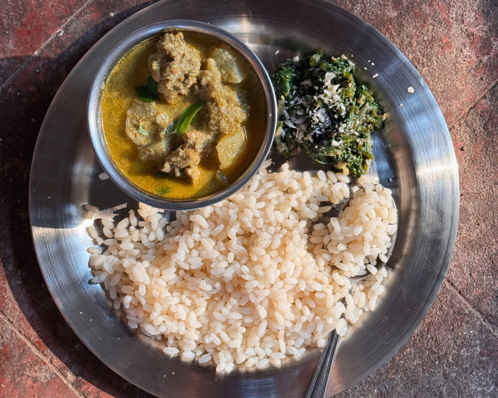 A steel plate with a bowl of Mangalorean green chicken curry, a side of coconut greens, and boiled rice, photographed from above on a red tiled floor.