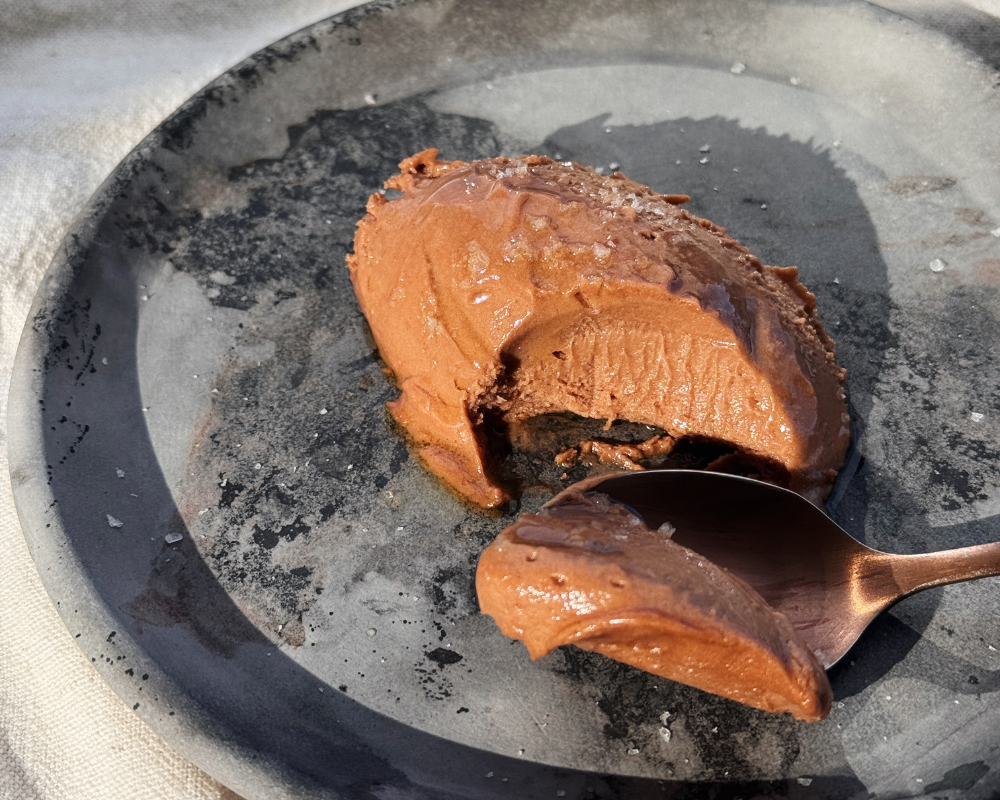 Hazelnut chocolate mousse with sea salt flakes on a dark ceramic plate with a spoon 