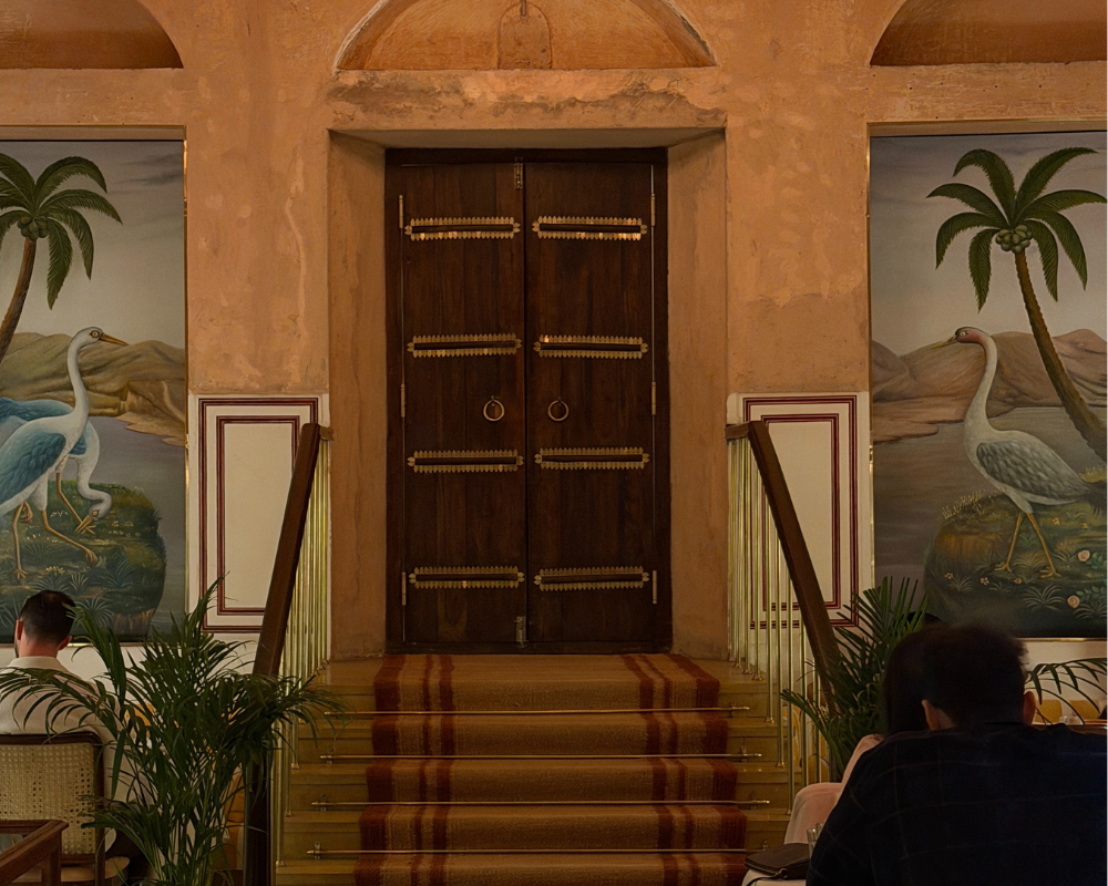  Ornate wooden doors framed by hand-painted bird murals at the entrance of The Johri Restaurant, Jaipur. 