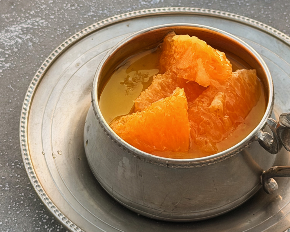 Close up of orange segments soaked in olive oil on top of Greek yoghurt panna cotta in a vintage silver cup 