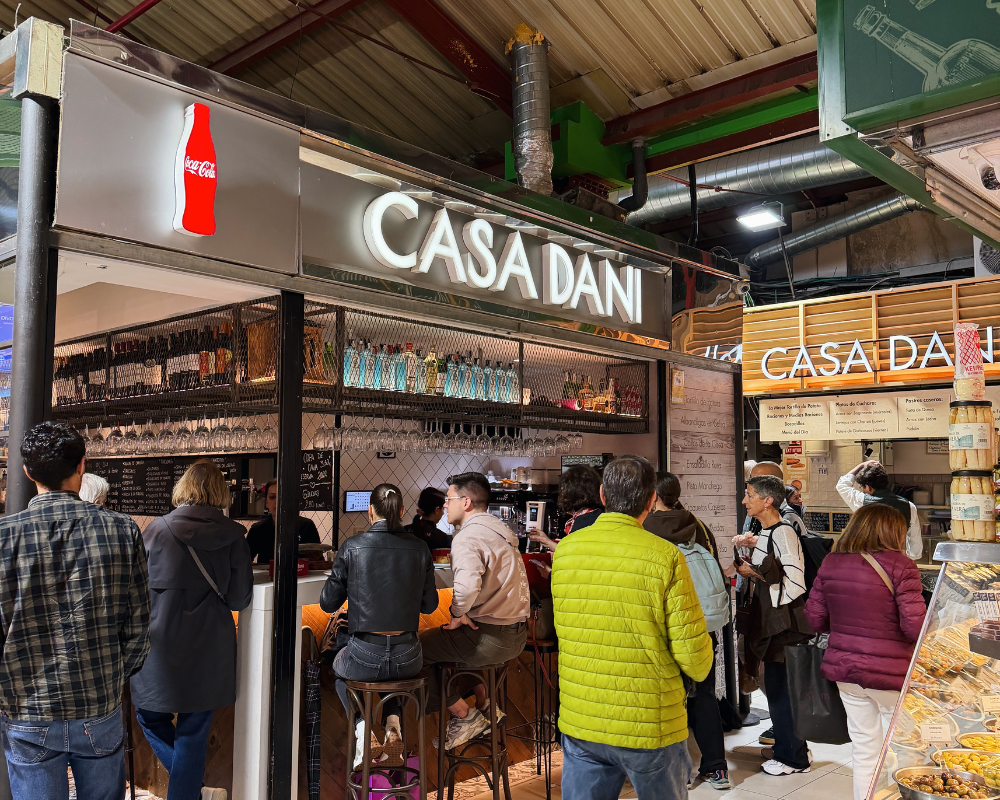  Customers seated at the busy counter of Casa Dani inside a Madrid market hall. 