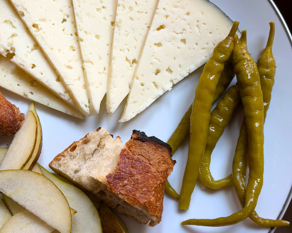  A white plate of sliced manchego, pickled green peppers, toasted bread and fresh pear in Madrid 